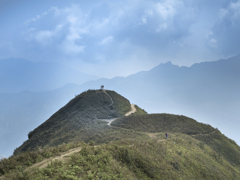 Scenic Rajmachi hilltop trail with lush green ridges, misty mountains, and visitors enjoying panoramic valley views.