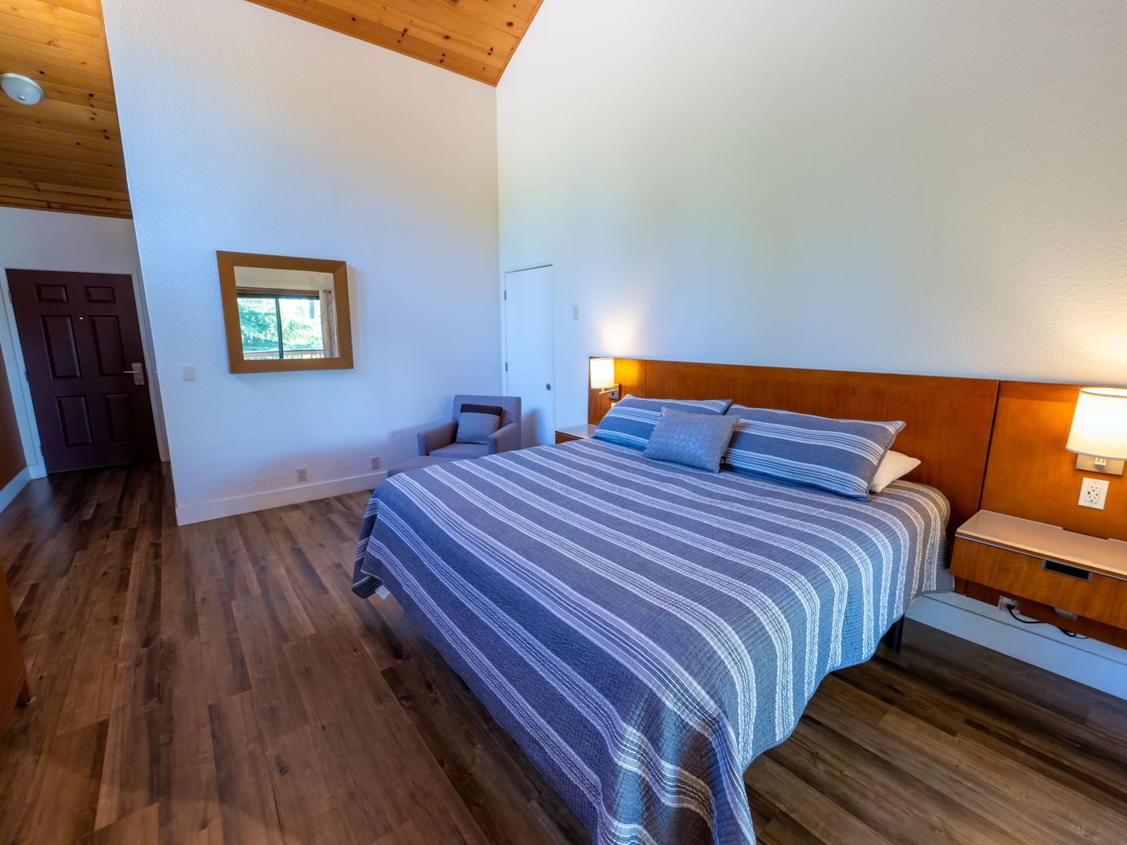 Deluxe King Room at Amador Hotel with a king-sized bed, wooden flooring, wall lamps, and a mirror above a dresser.