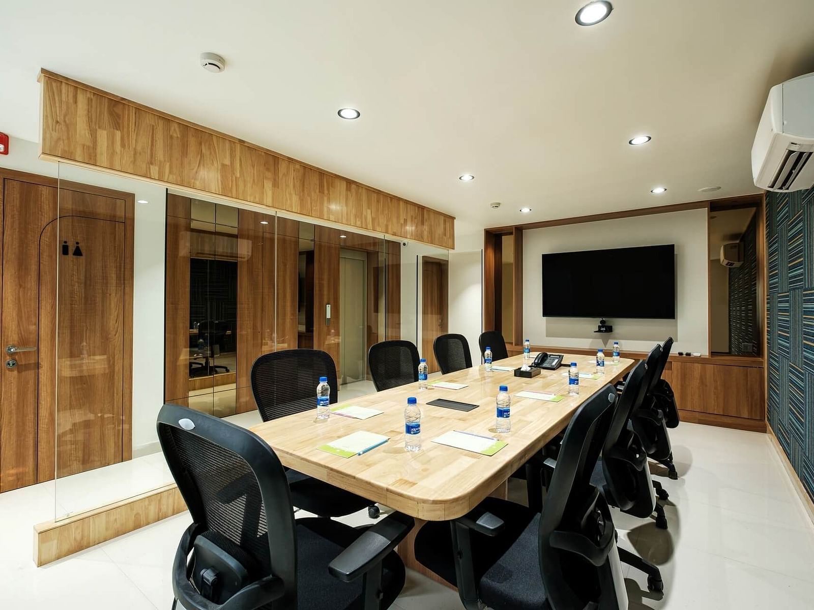 Diagonal view of the full boardroom at Indie Stays, Jaipur, with chairs along the sides, a screen at the front, and a wall-mounted AC.
