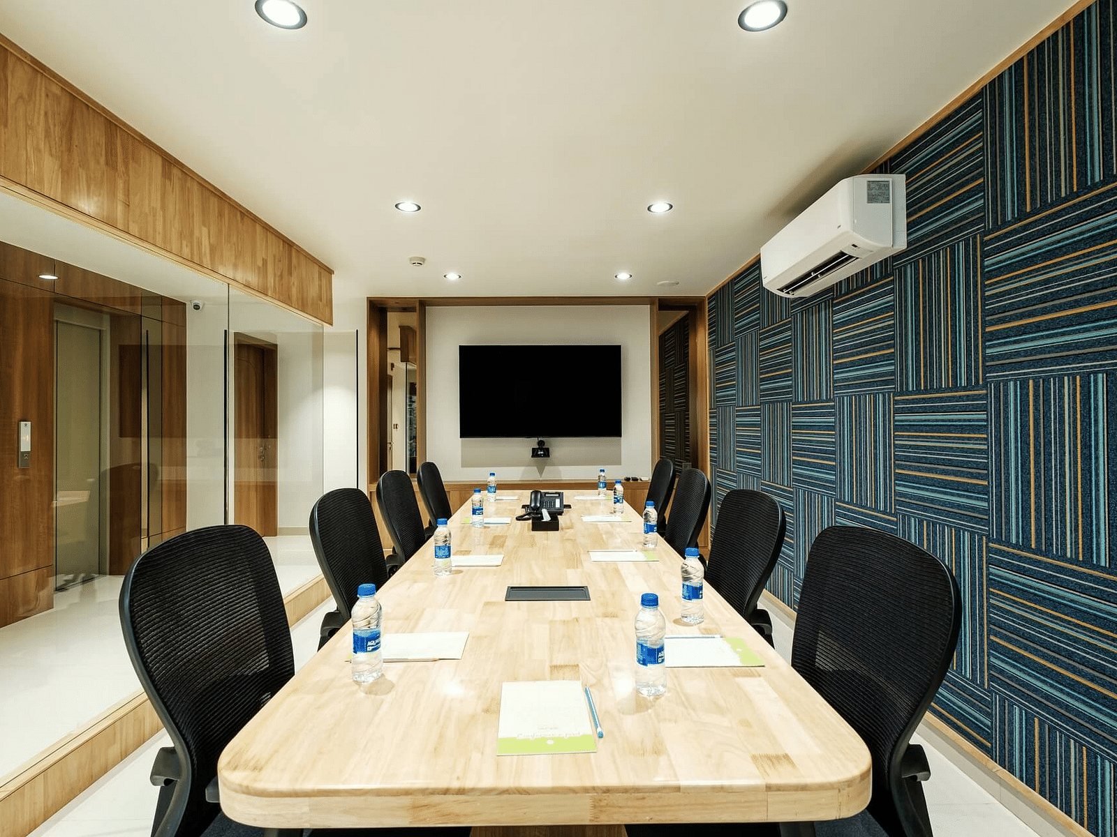  View of the full boardroom at Indie Stays, Jaipur, with chairs arranged along the sides, a screen at the front, and a wall-mounted AC.