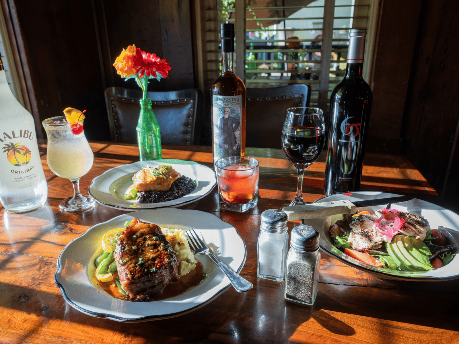 Three plates of food placed on a table at Tallman Hotel alongside bottles of beverage, floral decor and seasoning shakers