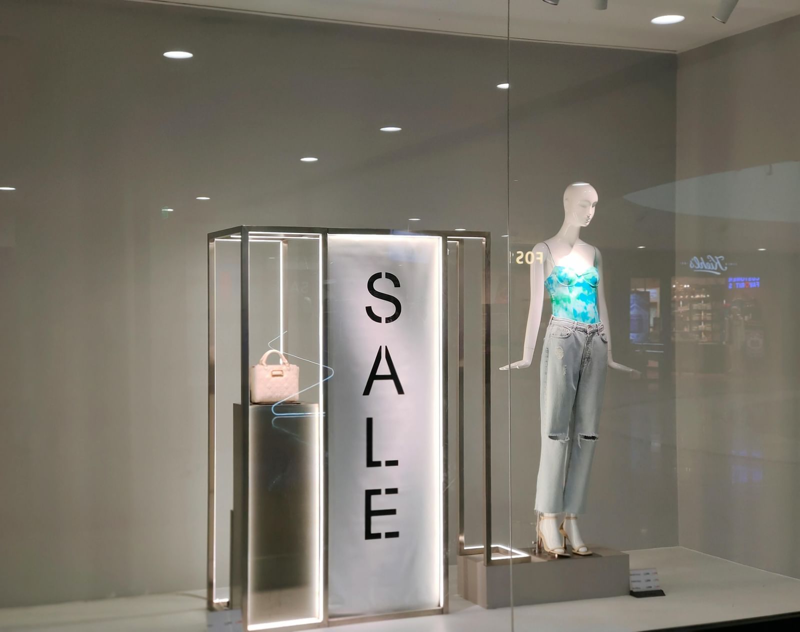 A mannequin stands in a storefront display next to a sign that reads 'Sale'.