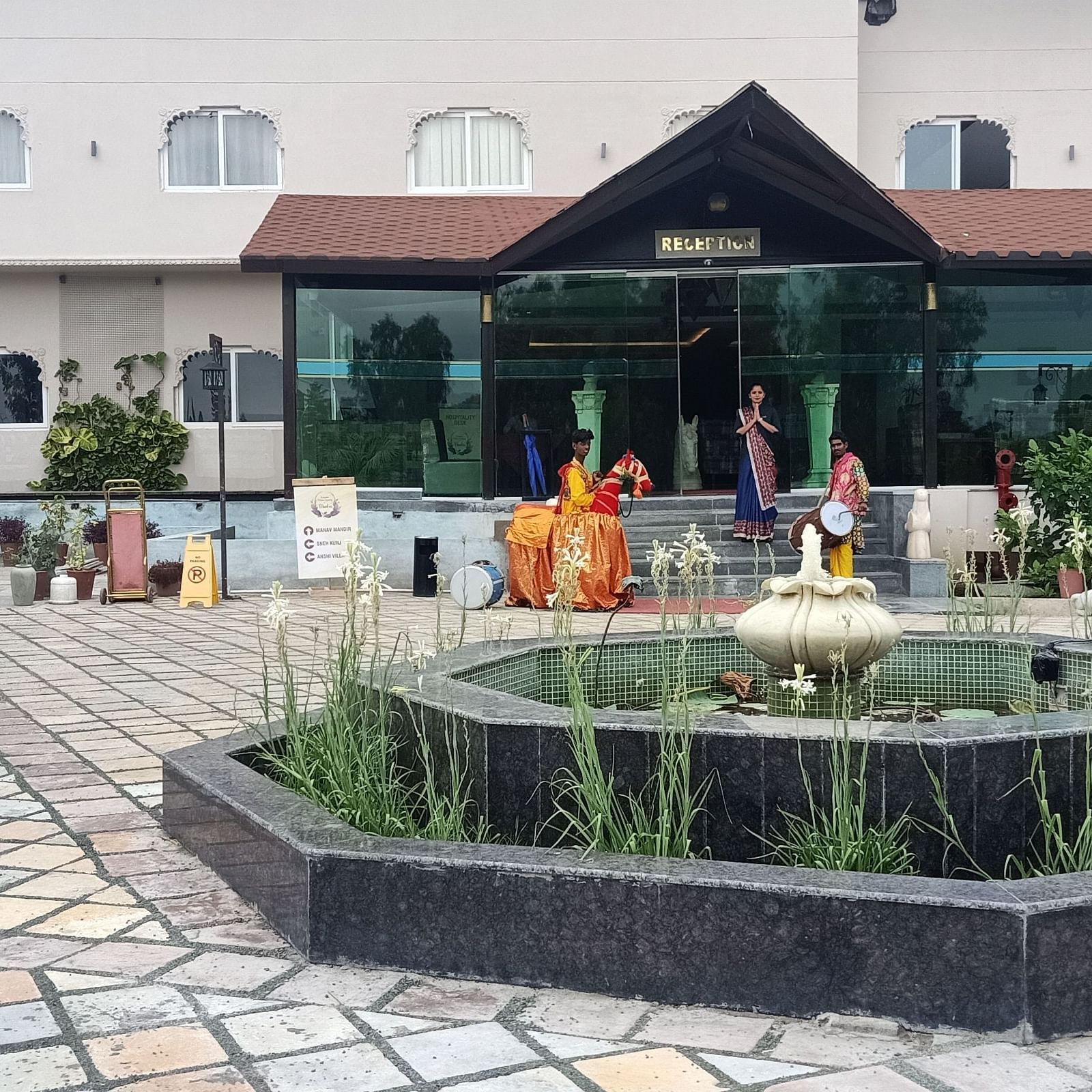A building with a covered entrance and a decorative fountain in a paved courtyard.- Bamboo Saa Resort & Spa, Udaipur