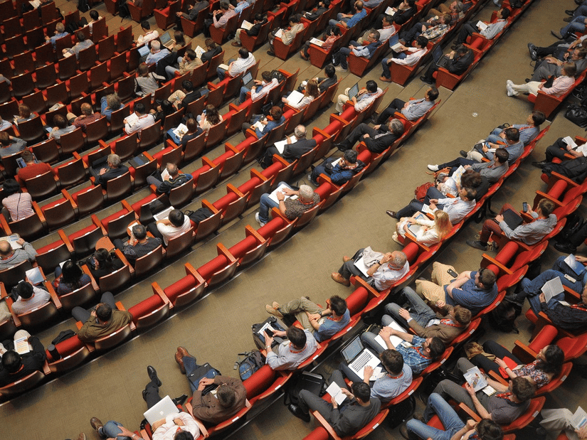 High-angle view of a large audience seated in rows of red theatre chairs during an event or performance.