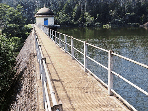 A dam with a walkway along the side, surrounded by dense forested hills and water below, signifying Aliyar Dam, one of the best places to see in Coimbatore.