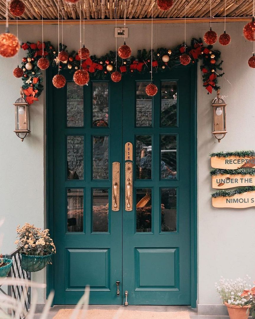 Decorated green double doors with hanging red ornaments and festive garland; and signboards placed on the wall beside - Karma Chalets