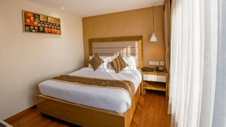 A bright and neatly arranged standard hotel room with a comfortable bed, a small desk, and an abstract painting above the bed at Yashshree The Imperial Inn, Siliguri