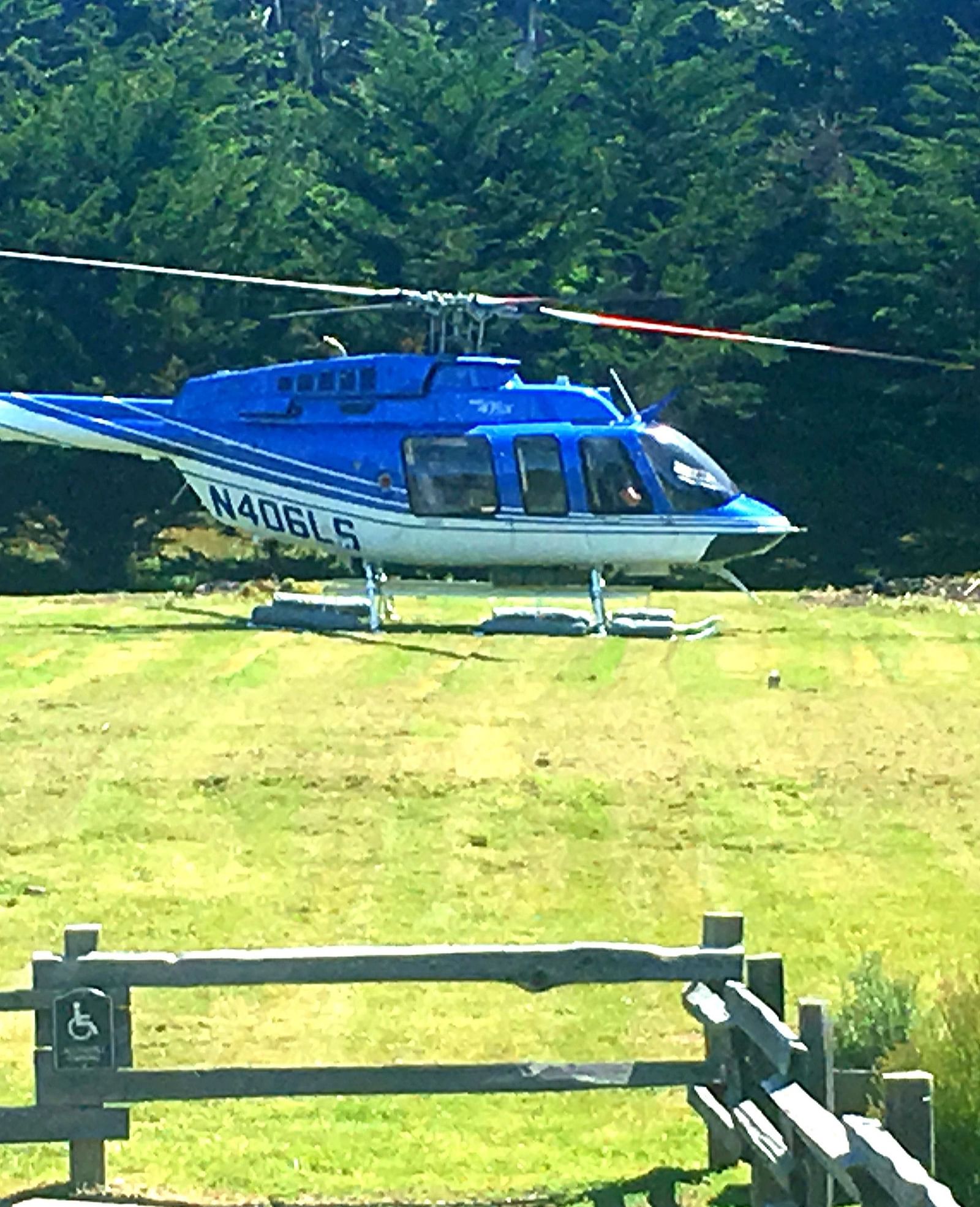 A blue coloured helicopter landing on a vibrant green field - Brewery Gulch Inn & Spa