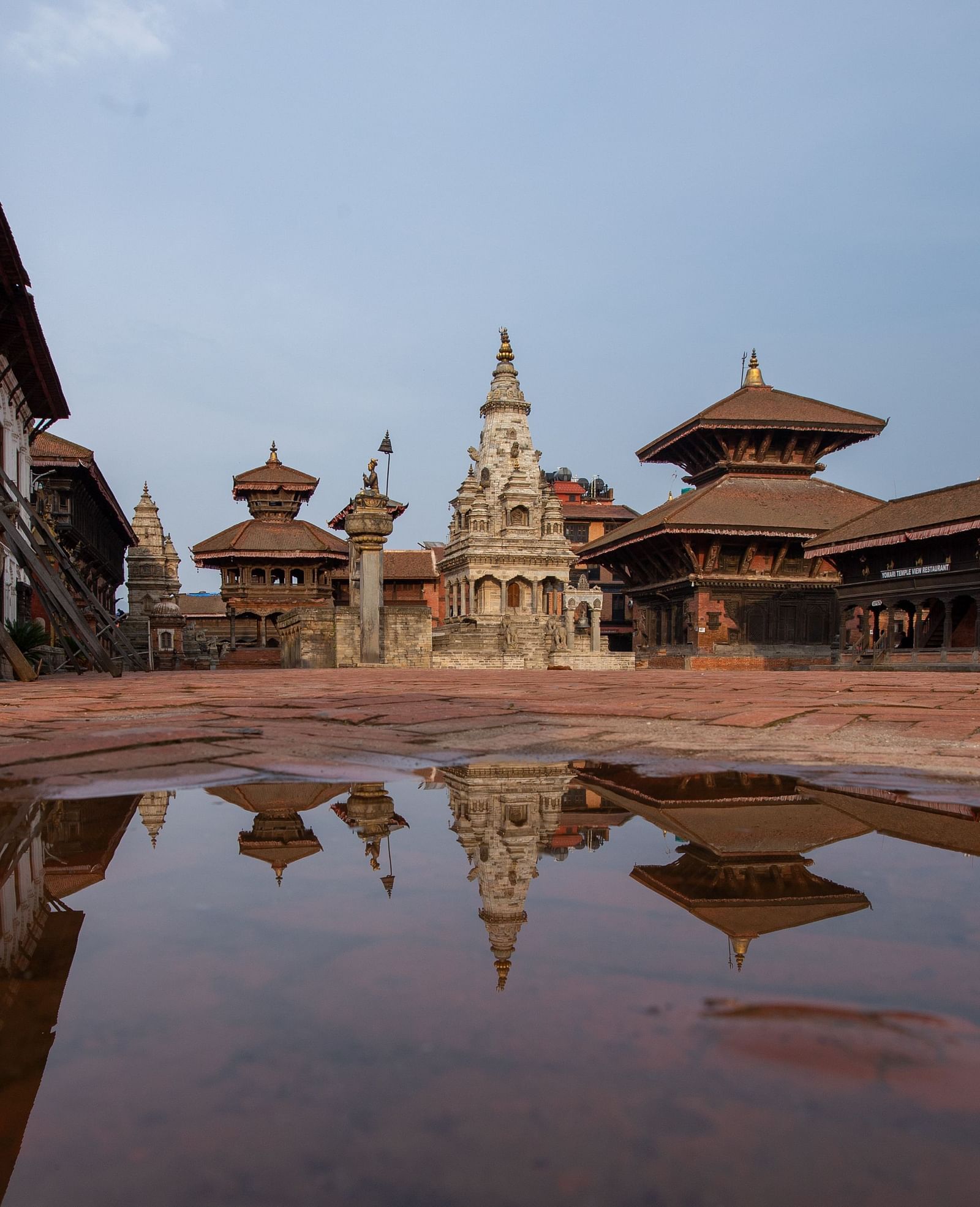A facade view of the bhaktapur durbar square where a puddle of water is reflecting the structure