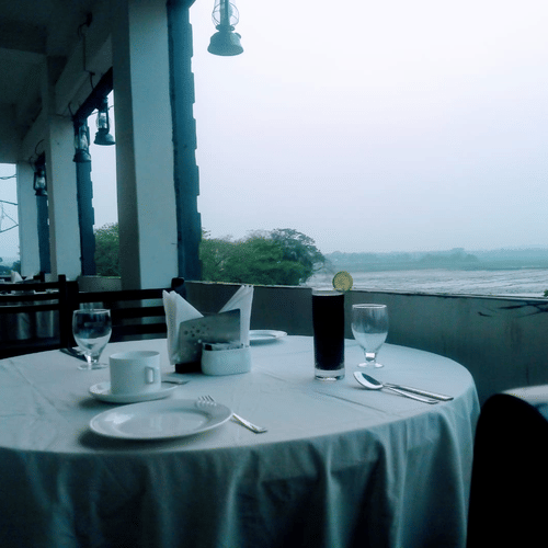 A dining space with an outdoor view featuring a round table covered in white table cloth and set with plates