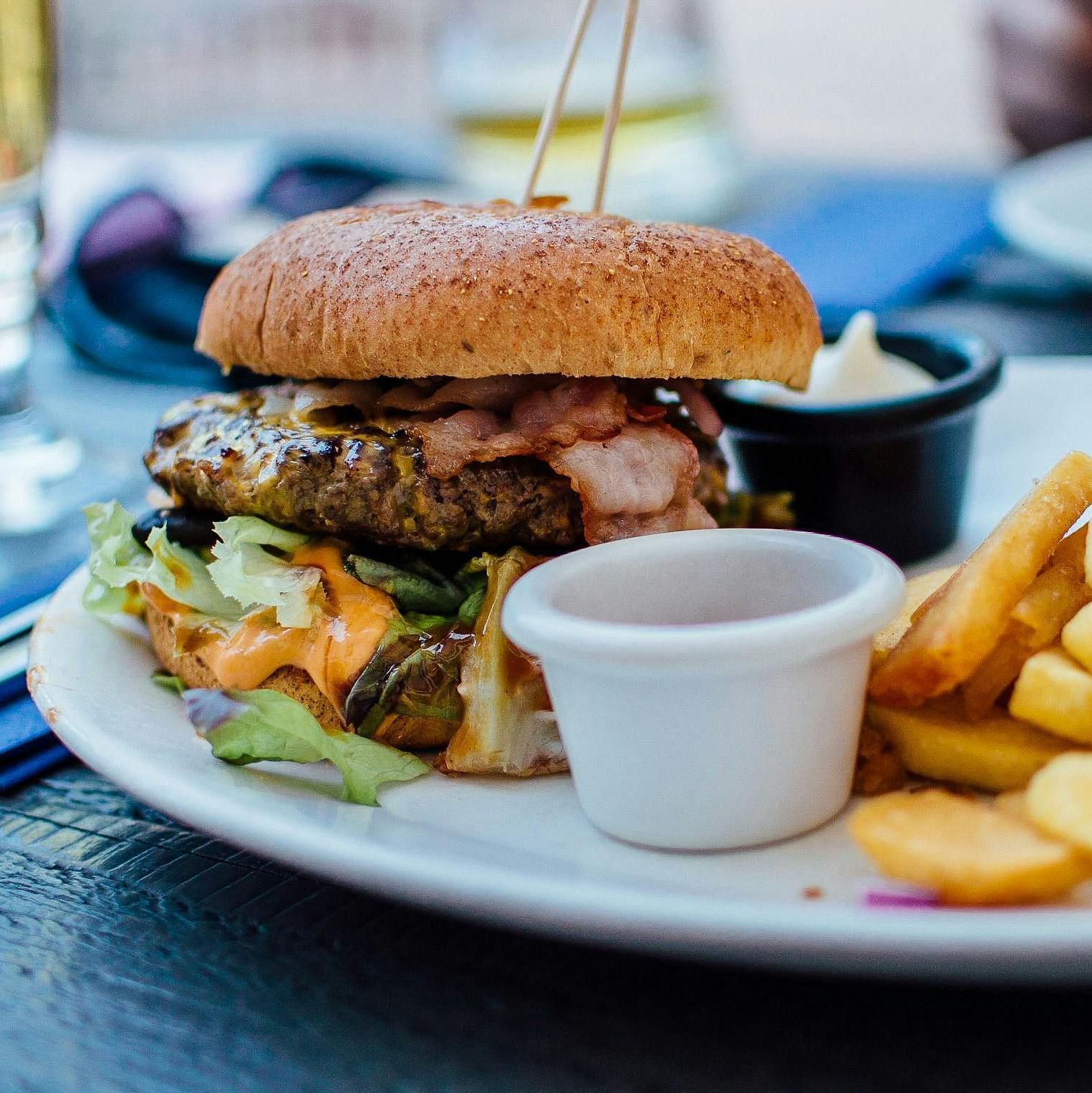 A plate of burger with fries placed in a wooden table in an outdoor arrangement