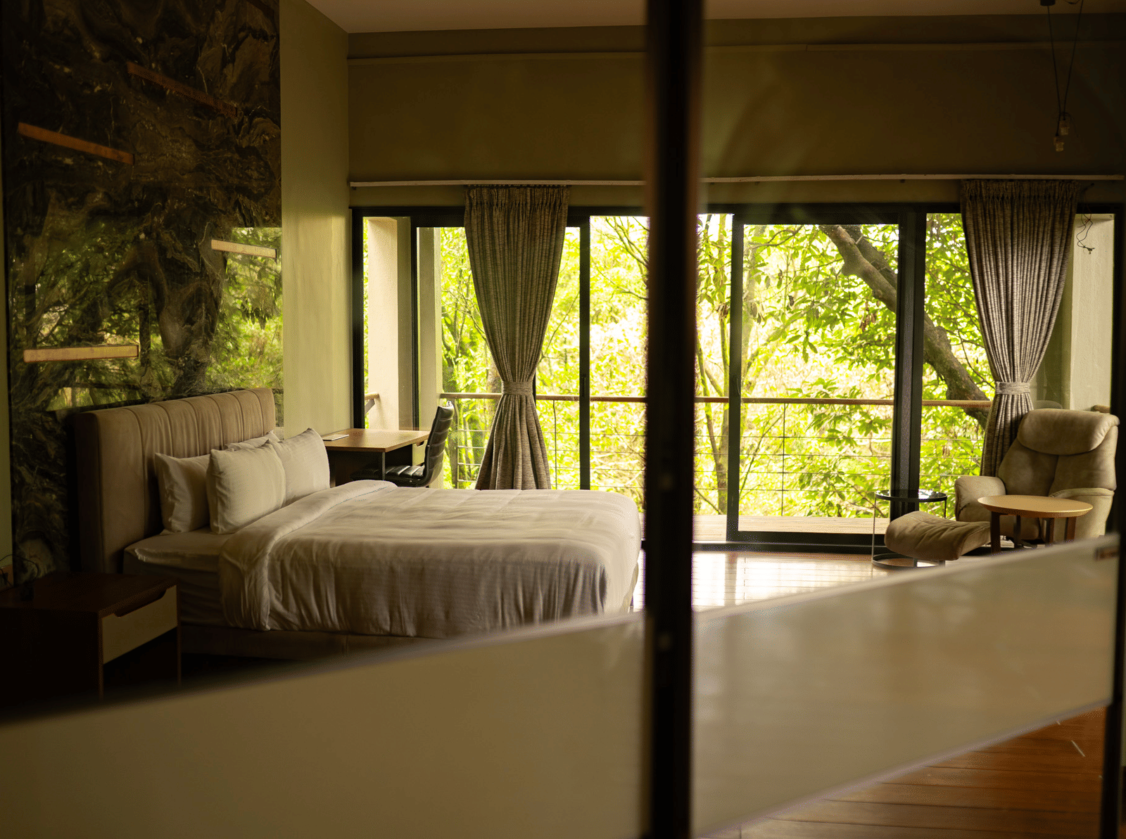 A bedroom at Stanley Revelation with a large bed, seating, and a balcony overlooking a forest.