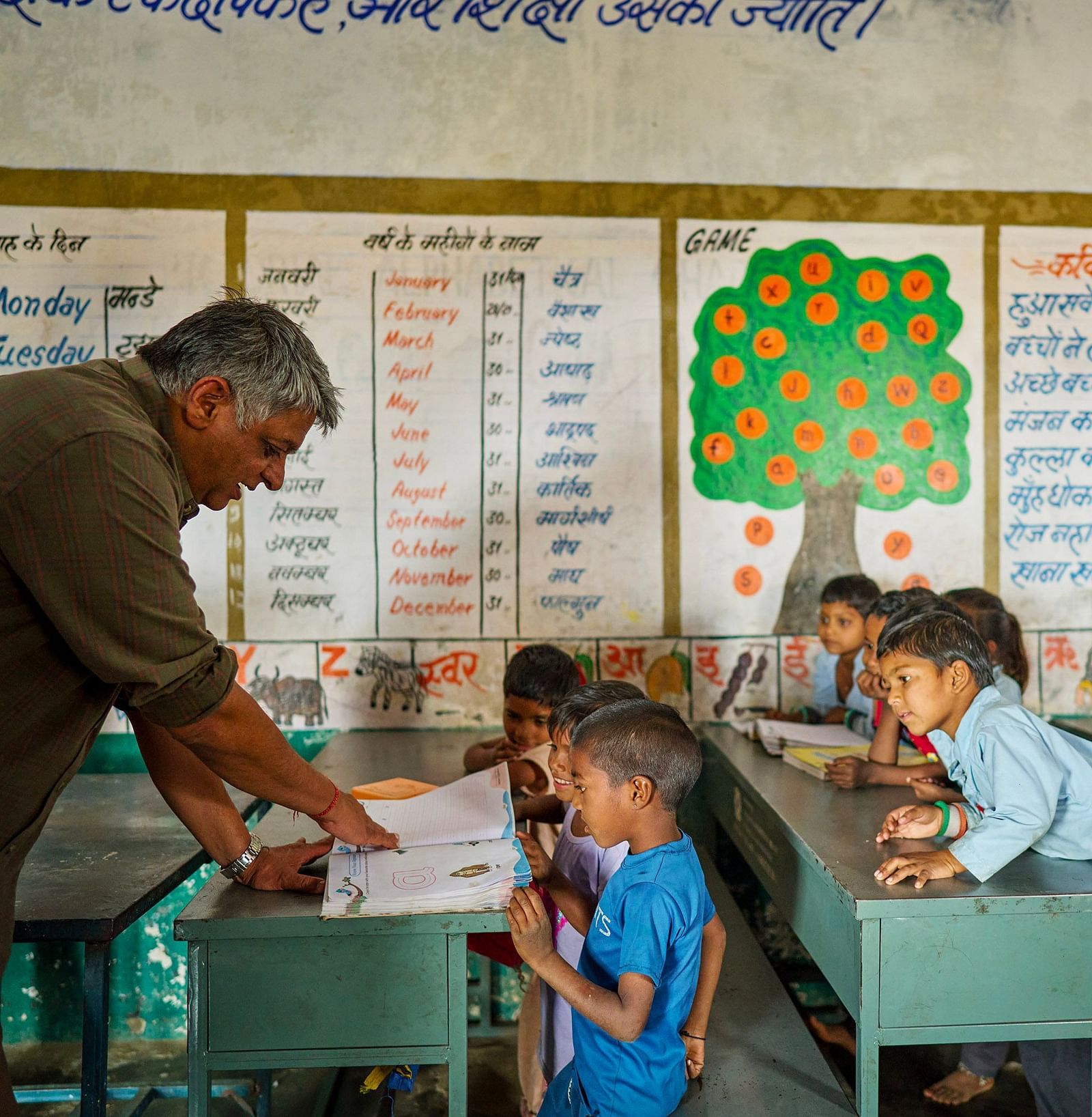 image of an old man teaching the children through a textbook at deogarh