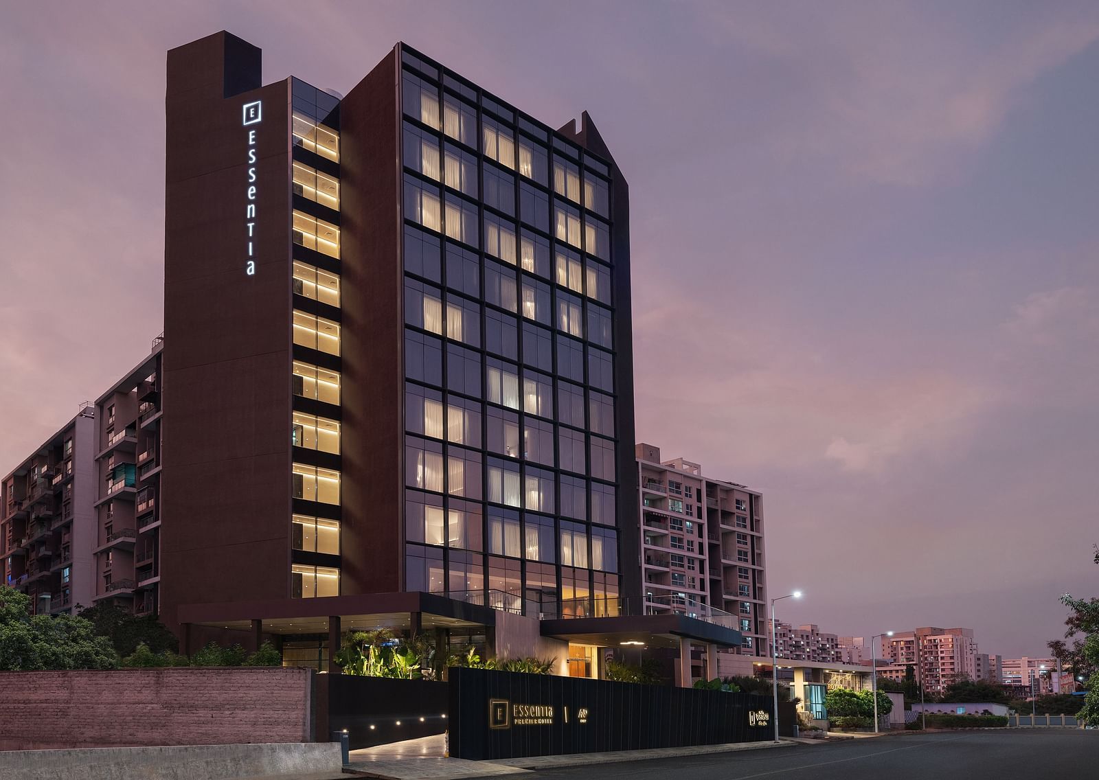 Facade of Essentia Premiere, Pune with lights on during twilight.