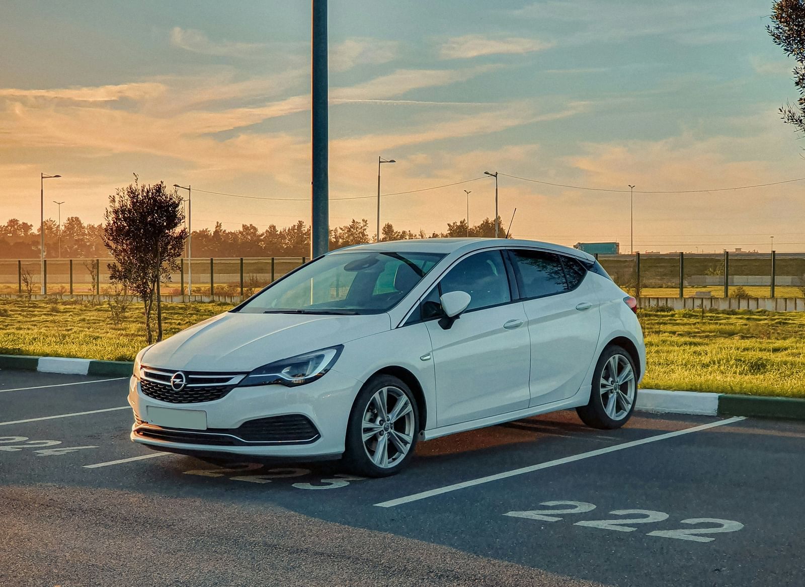 A pristine white car parked in a car park at dusk, with sunlight casting warm hues.