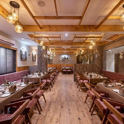 A dining area with multiple tables and chairs set for meals along a corridor with a wooden theme at Angel Lords Eco Inn Amreli.
