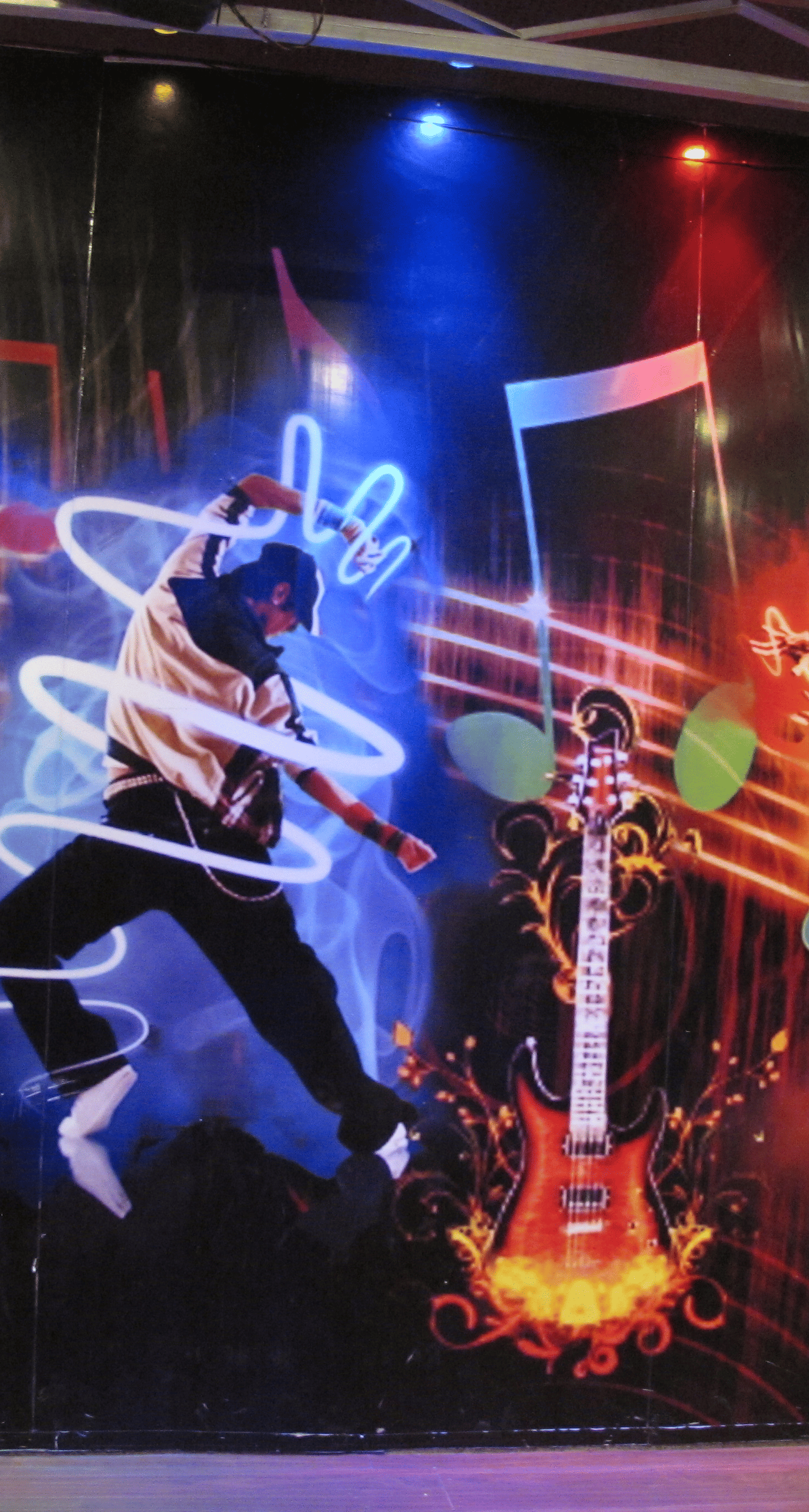 A close-up view of the wall mural, showcasing energetic dancers and dynamic light effects - TGI Apple Inn, Jaipur 