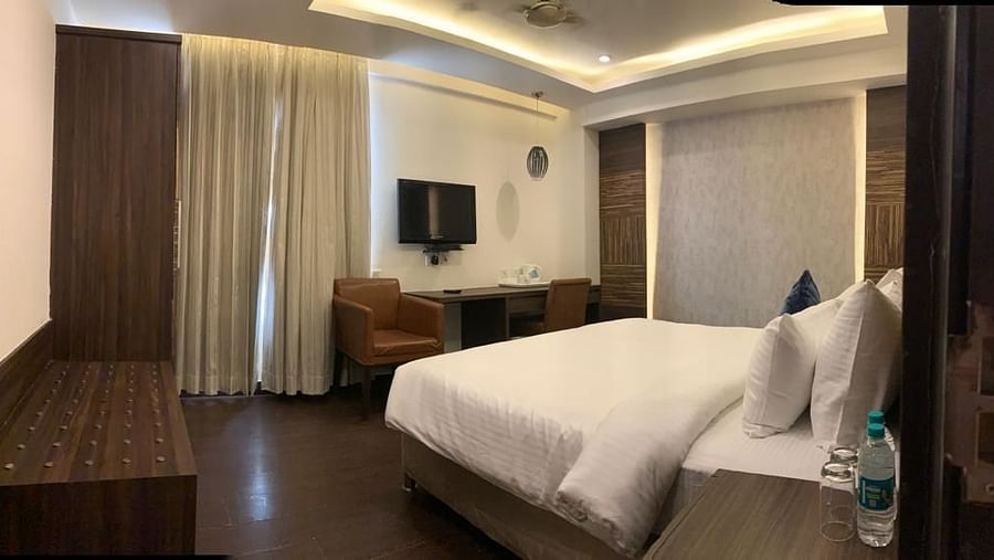 A bedroom with a white bed, a brown sofa, and a decorative ceiling with inset lighting - VITS Gurugram
