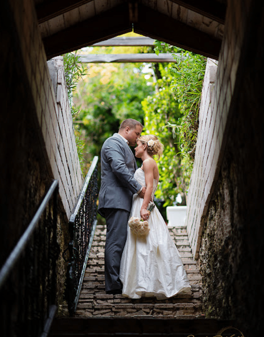 A couple standing in a narrow stone stairway tunnel, embracing each other under natural light | A Stone's Throw Away