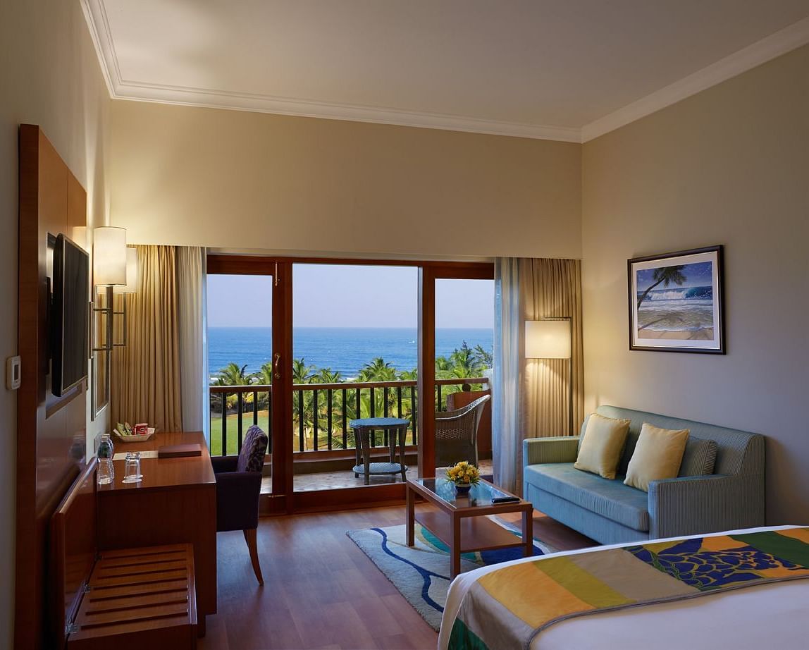 a double bed with a sofa, table, lamps and tv in view inside Ocean front view - Caravela Beach Resort Goa