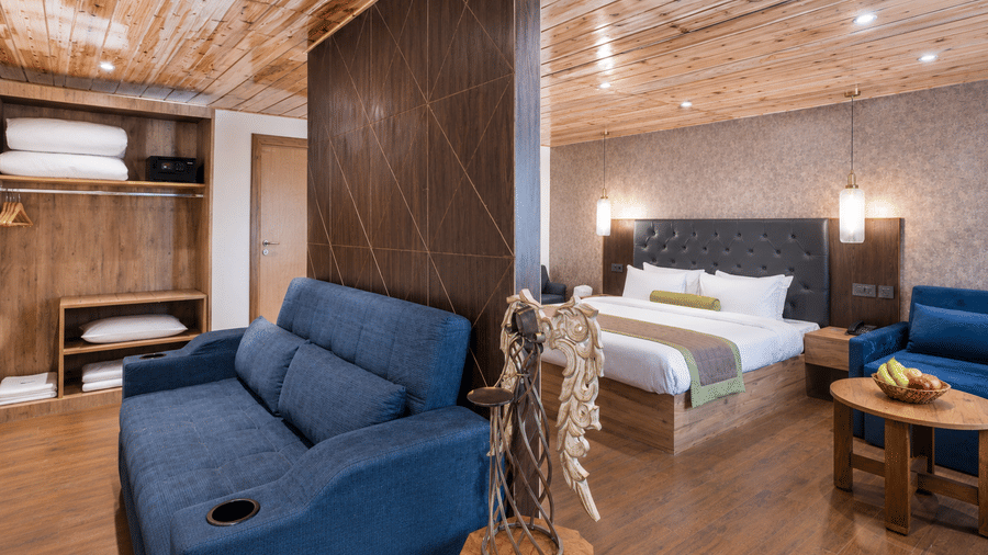 King Suite at Valmere Magnolia Boutique Hotel & Spa, Pelling with a navy sofa, an open wardrobe, a decorative wooden sculpture, and a bed with a nearby fruit bowl.
