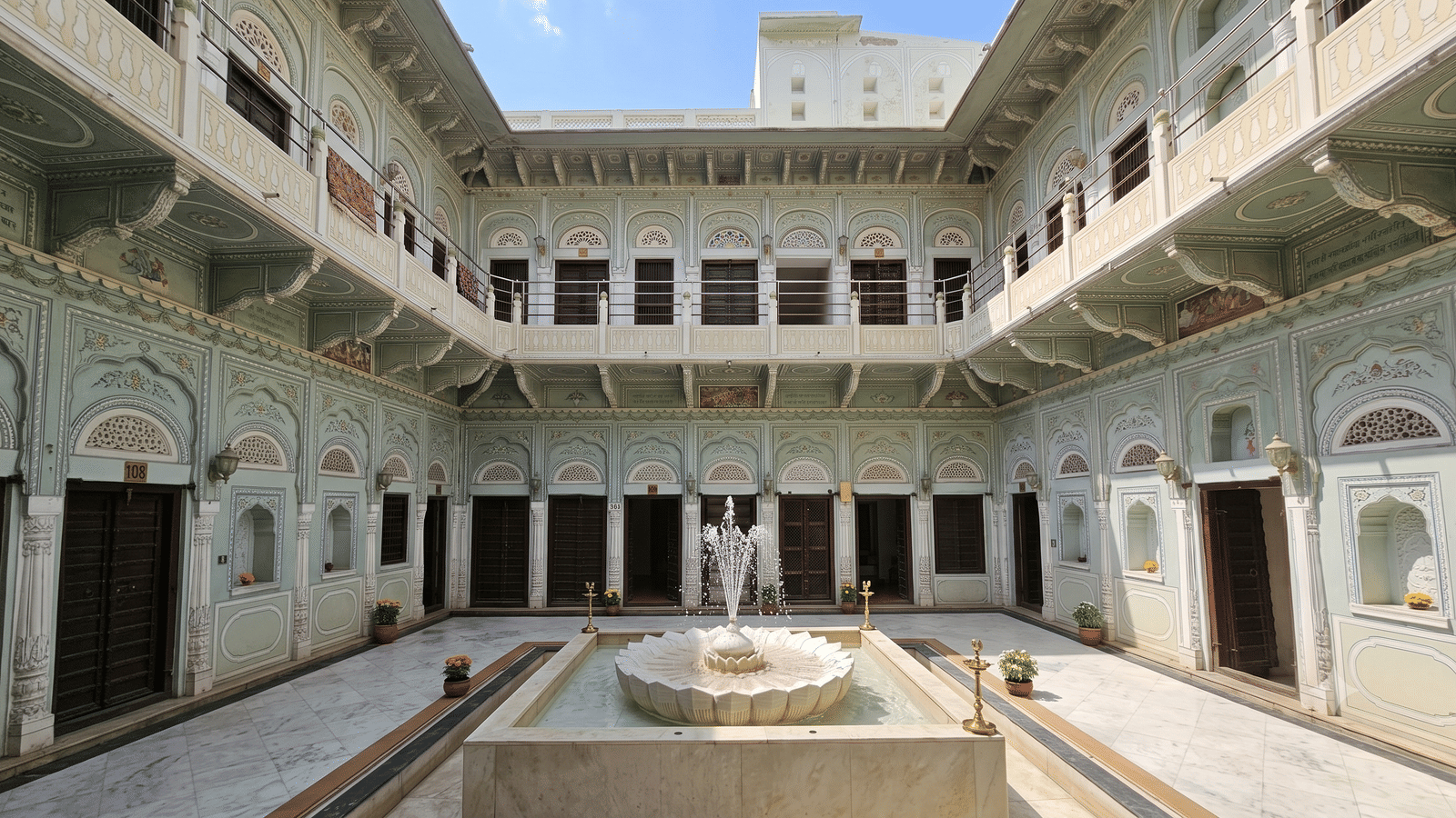 Three-storey painted courtyard with arched galleries, a marble lotus fountain and potted marigolds under a clear sky at BluSalzz Vintage - Harlalka Haveli.