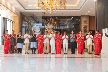Group of hotel staff and management posing in a grand lobby with red-themed uniforms.