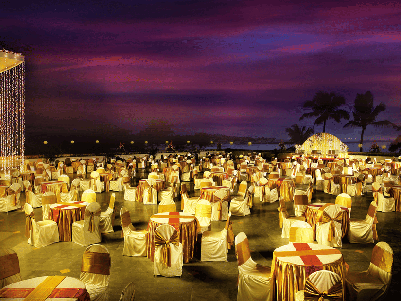 A large outdoor event setup with round tables and chairs covered in cloth arranged under evening lighting.