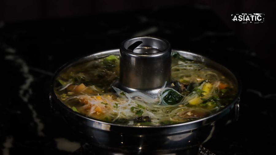 Metal pot with vegetables and broth on a black counter at Asiatic Lounge.