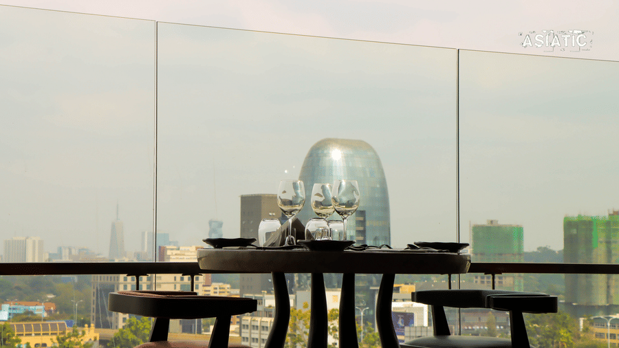 A table with glass dome covers over food trays set on an outdoor terrace, with a city skyline in the background at Asiatic Rooftop Bar and Restaurant.