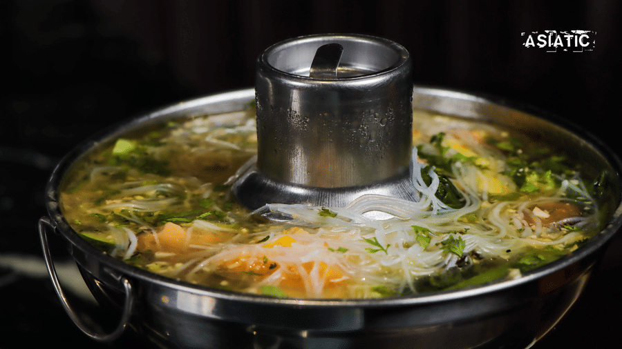 A close view of a metal pot with vegetables and broth cooking at Asiatic Rooftop Bar and Restaurant.