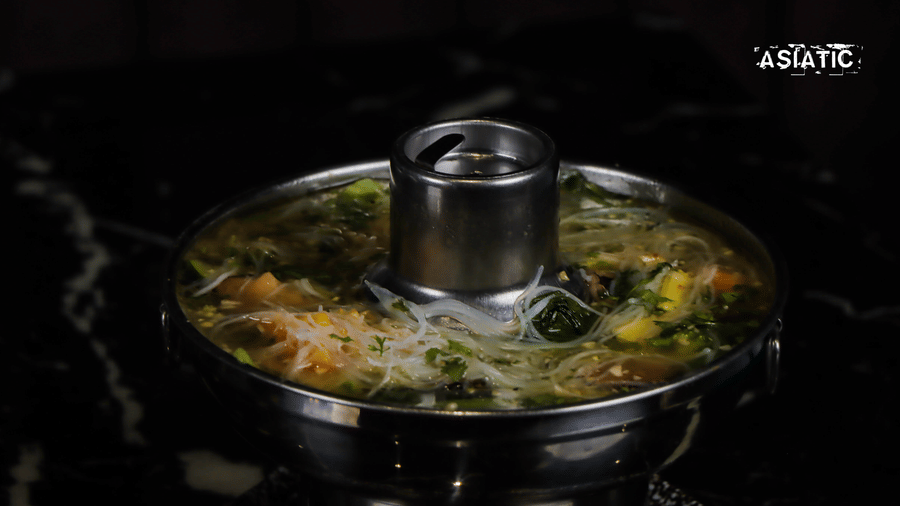 Metal pot with vegetables and broth on a black counter at Asiatic Rooftop Bar and Restaurant.