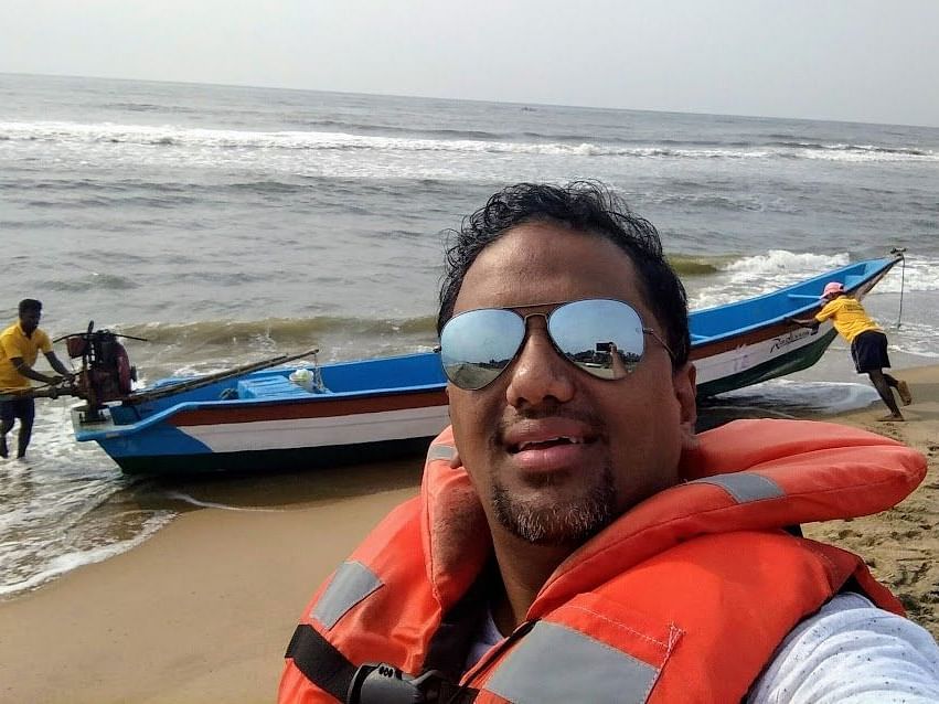 A person taking a selfie in front of a boat at the beach.