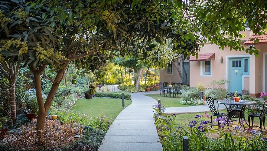 Walkway through a garden with trees and outdoor seating, leading to a light-coloured house in the background at Karma Chalets.