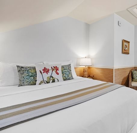 A room with bed, white walls, and floral themed pillows at Hartstone Inn.