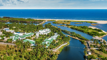 A scenic aerial view of Radisson Resort Pondicherry Bay showing lush greenery, winding waterways and the coastline promoting the Winter Waves meeting offer.