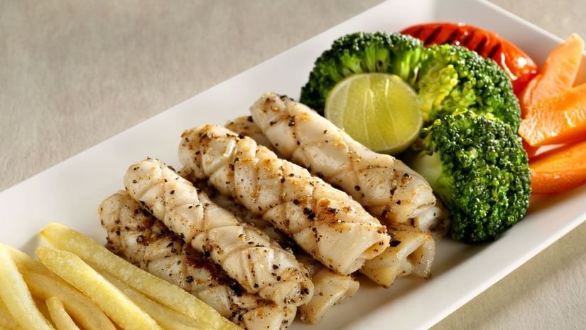 Grilled fish fillets served with golden chips, steamed broccoli, carrots, tomatoes, and a fresh lemon wedge for garnish on a plate - Abad Plaza, MG Road, Shenoy Kochi