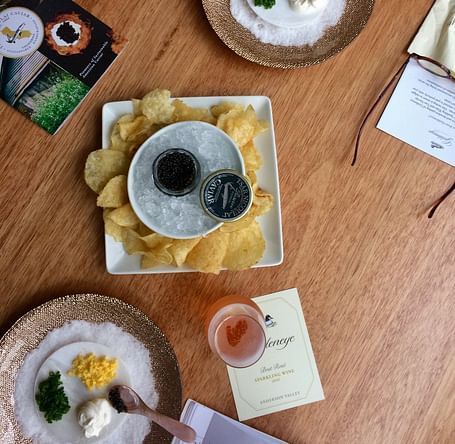 An image of a dinner table where several plates are placed with food items on it like chips, scarmbled eggs, leafy vegetables, cream, and some tapioca seeds