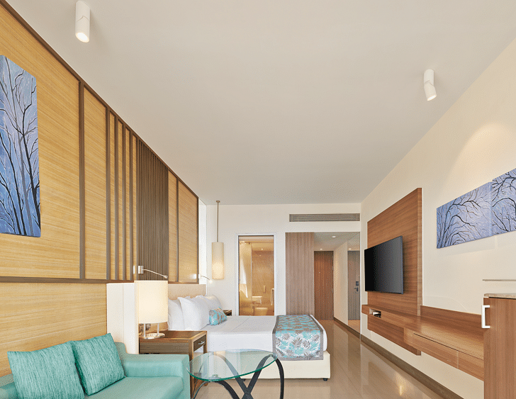 Stylish modern room with wooden accents, pastel furnishings, a wall-mounted TV and an open layout leading to a spacious ensuite – The Resort, Mumbai