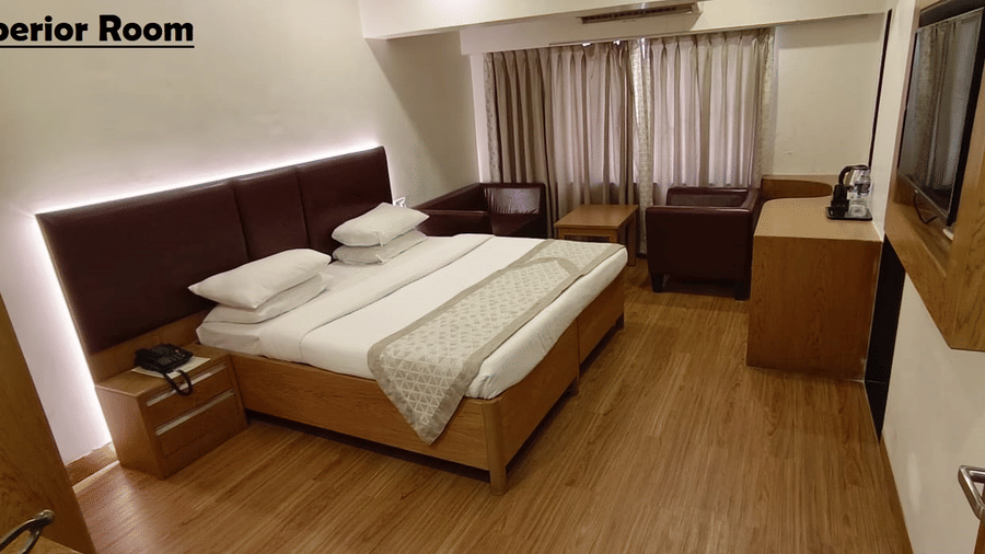 A Superior Room at Kings International Juhu with a bed, a flat screen TV facing the bed, a nightstand and an A/C unit.