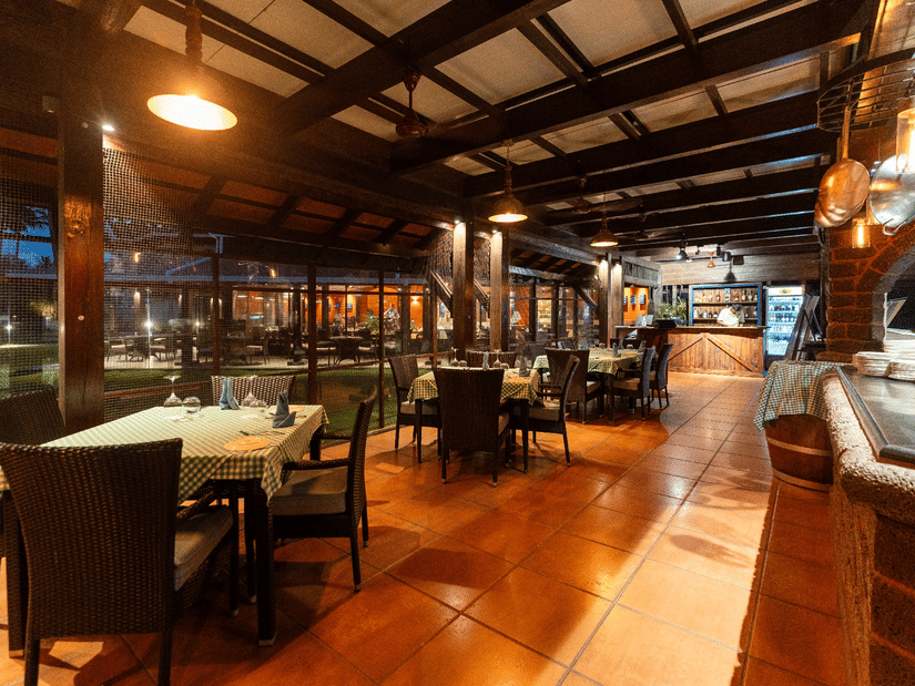 Warmly lit restaurant interior featuring wooden flooring, dining tables, ambient lighting and an inviting bar counter.
