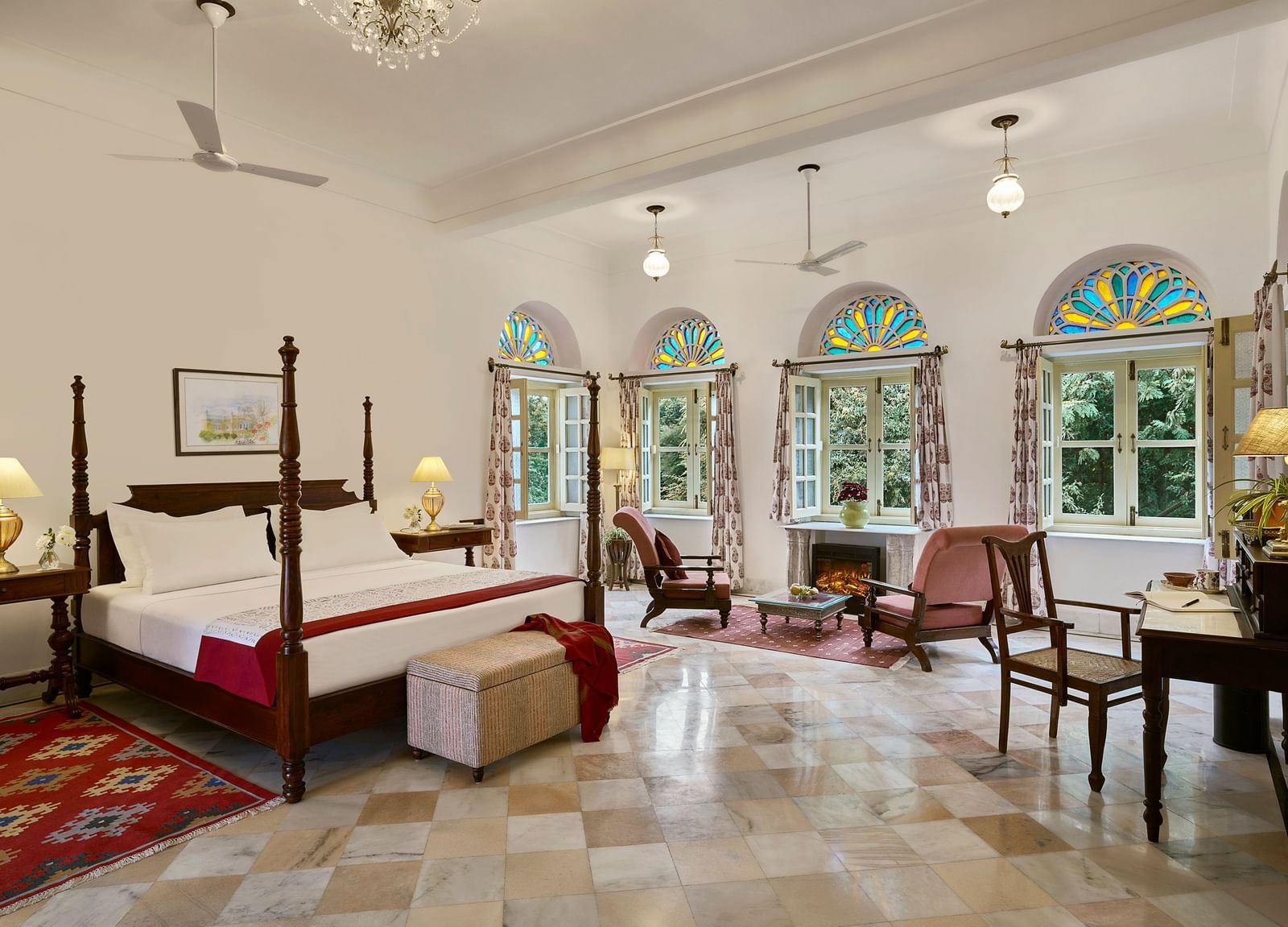 A suite featuring a large wooden bed and chairs arranged in front of the fireplace, set within a well-ventilated room at Dev Shree, Deogarh.