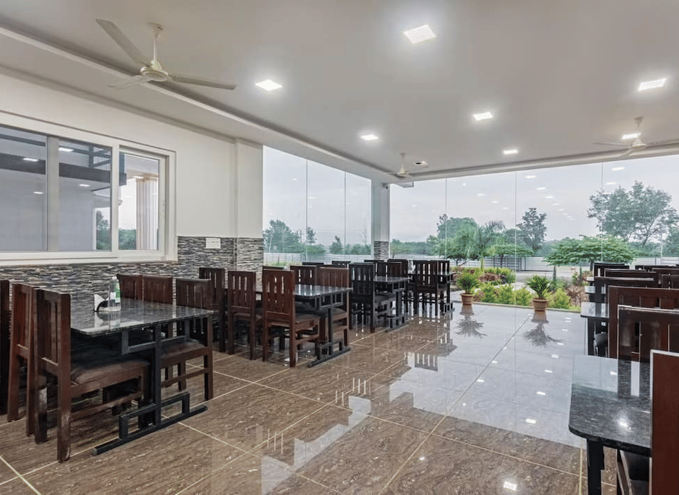 Well-lit restaurant with large windows offering scenic views and comfortable wooden seating at Siri Ambari Resorts and Spa.