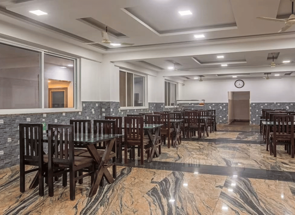 Indoor dining area with polished flooring and neatly arranged wooden tables and chairs at Siri Ambari Resorts and Spa.