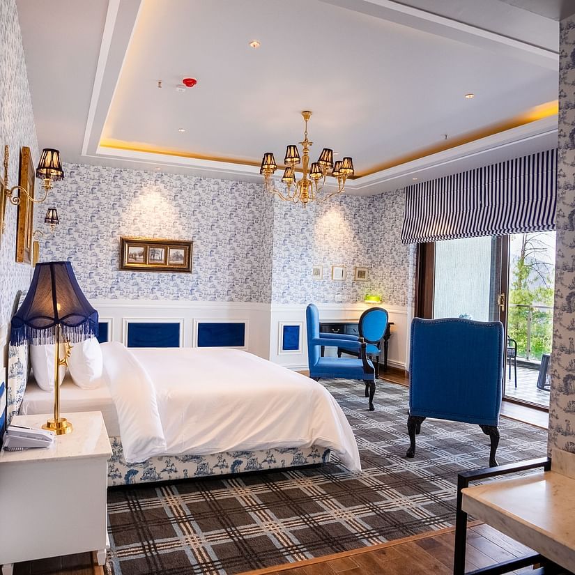 A hotel room with a large bed and comfy blue chairs  - The Manor Luxury Hotel, Shimla