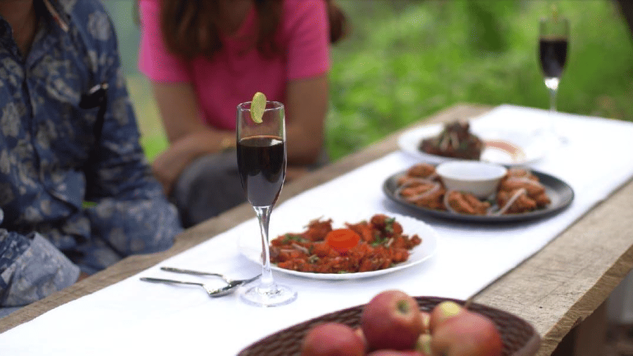 A close-up shot of a dining table cover with a white-coloured table cloth featuring several preparation and a glass of wine with shiny cutlery at Amara Upepo - The Sky Village, Manali.