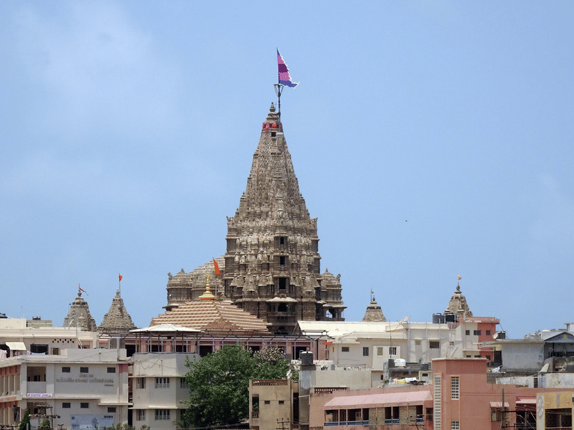 A temple with a tall spire and flag rising above surrounding buildings under a clear sky.