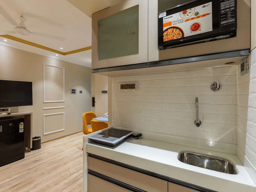 A well-equipped kitchenette at  Home2 Residency, Mumbai Airport, featuring a microwave, sink, and flat-top stove.