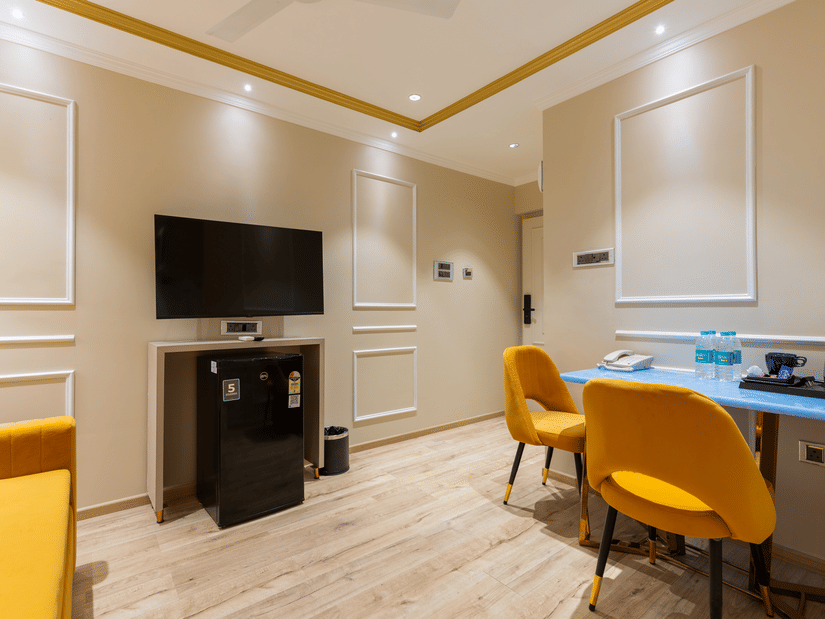 Interior view of a room at Home2 Residency, Mumbai Airport, featuring a wall-mounted TV, work desk, and vibrant yellow seating .