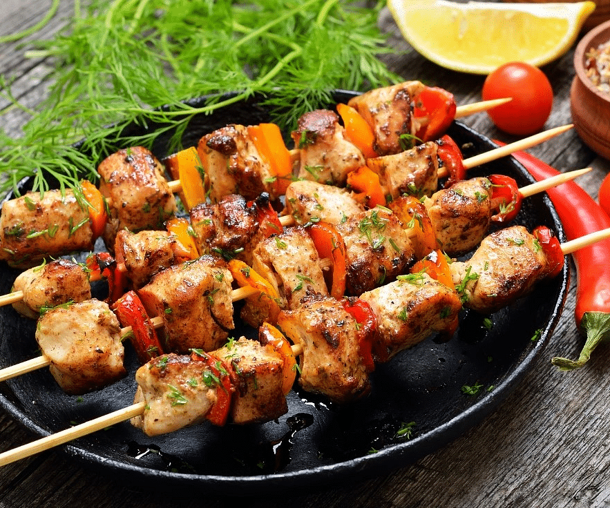 A close up shot of meat in a skewer with the ingredients kept next to it - Rhythm Gurugram